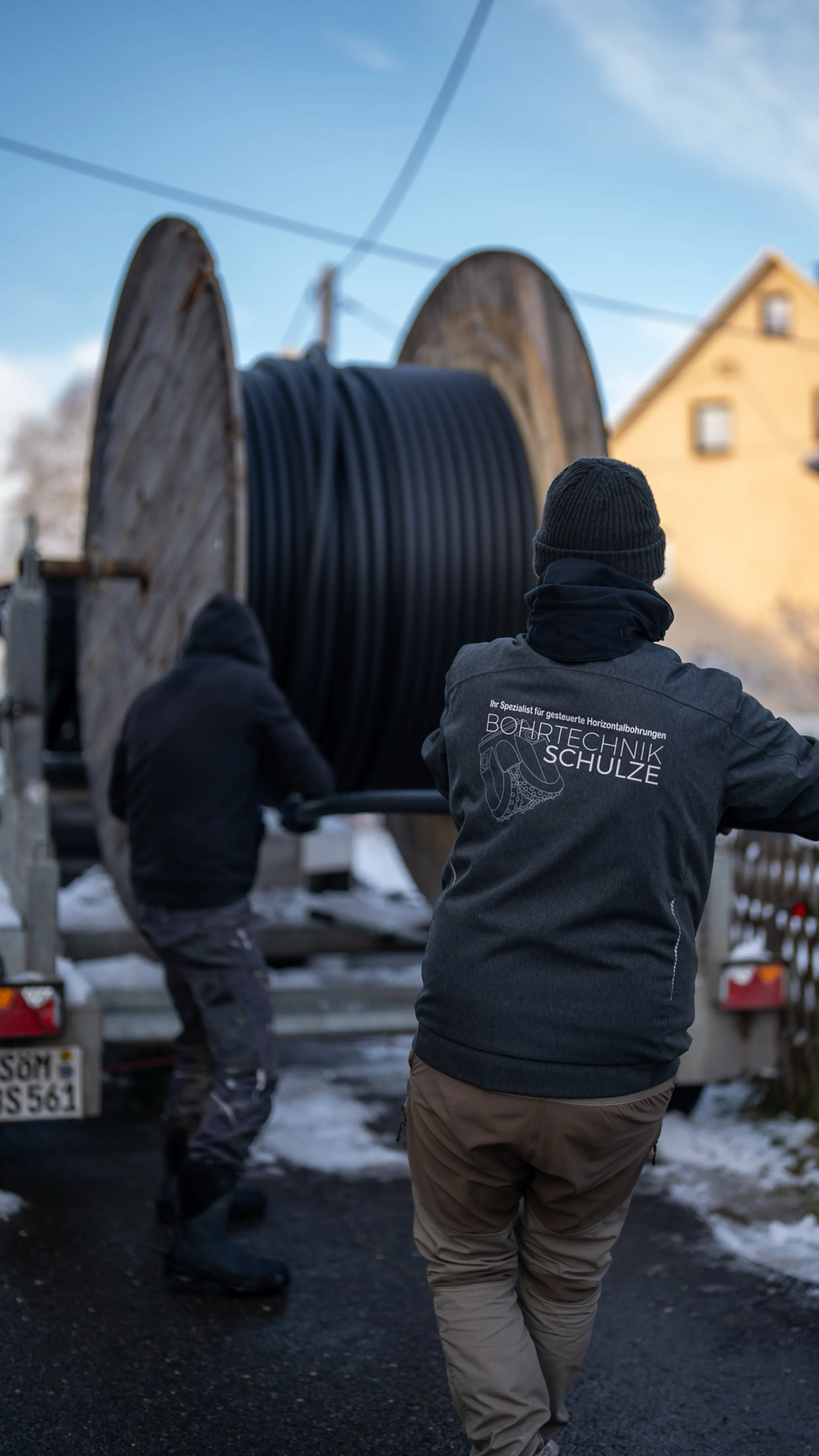 Zwei Mitarbeiter von Bohrtechnik Schulze von hinten an einer Kabeltrommel